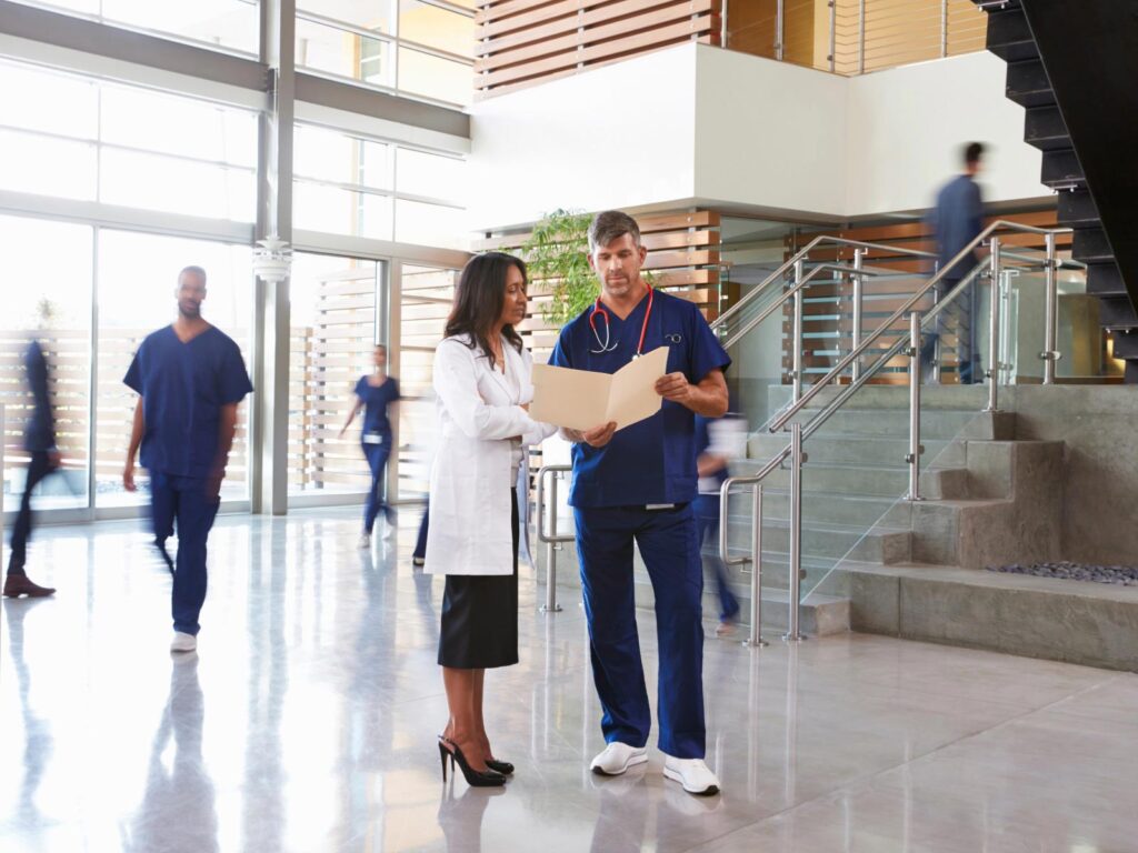 A man in scrubs consulting with a professionally dressed woman in a lobby.